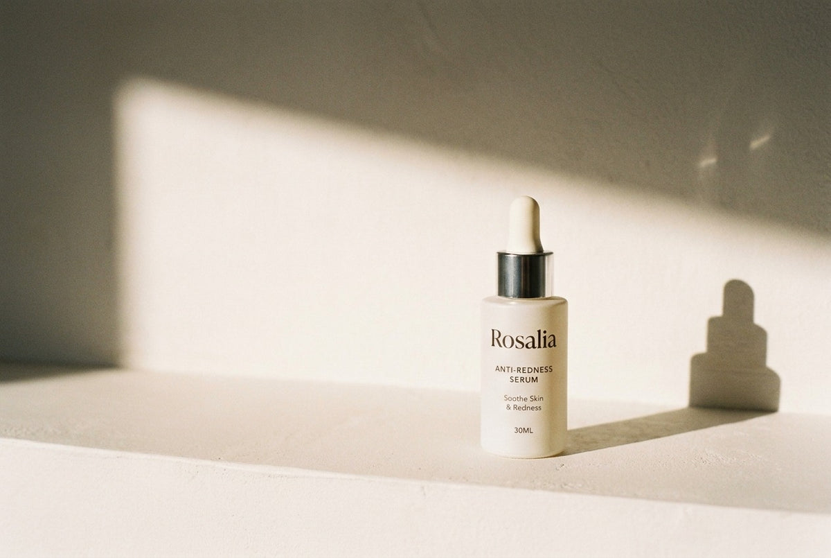 The Rosalia Anti-Redness Serum bottle standing alone on a plaster ledge in hard morning light