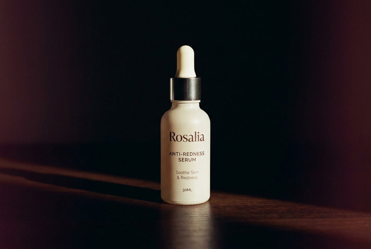 A close-up of the Daily Reset Serum under dramatic side light, deep wine and rose shadows, dropper poised.