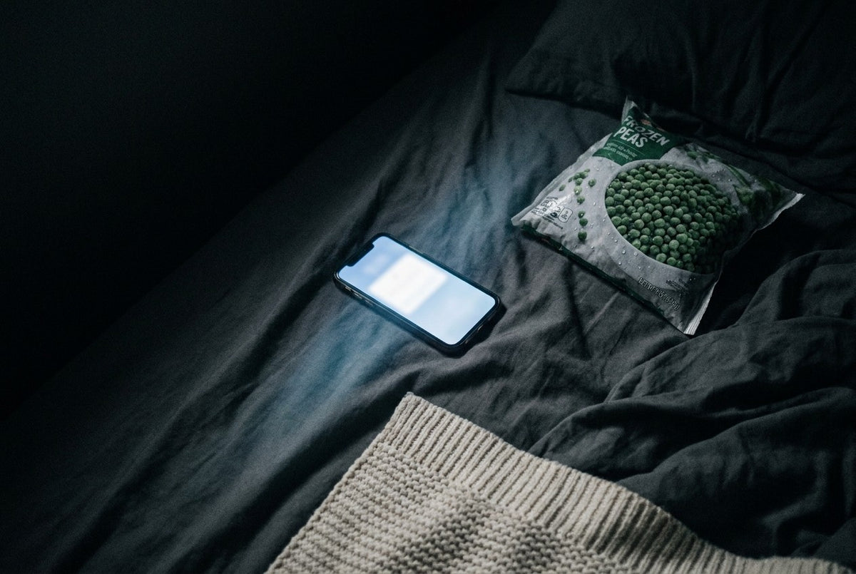 A phone lying screen-up on a dark bed, its screen the only light in the room